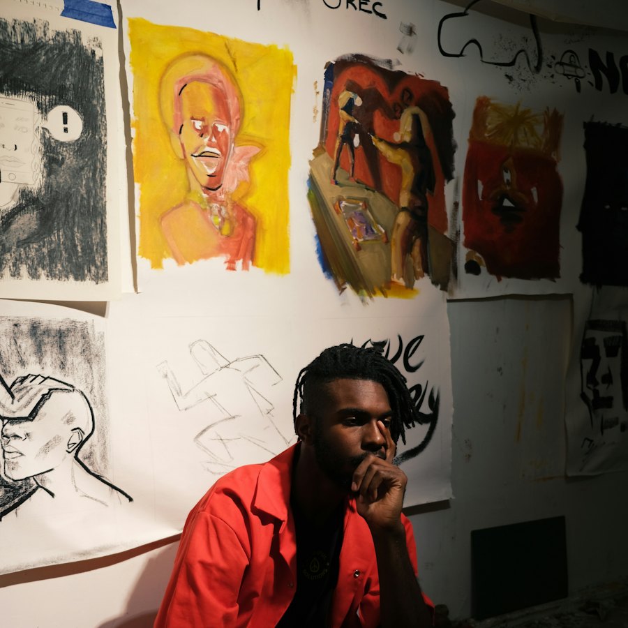 An artist sitting in a studio full of paintings